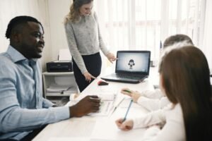 A diverse team collaborates during an office meeting with a laptop presentation.